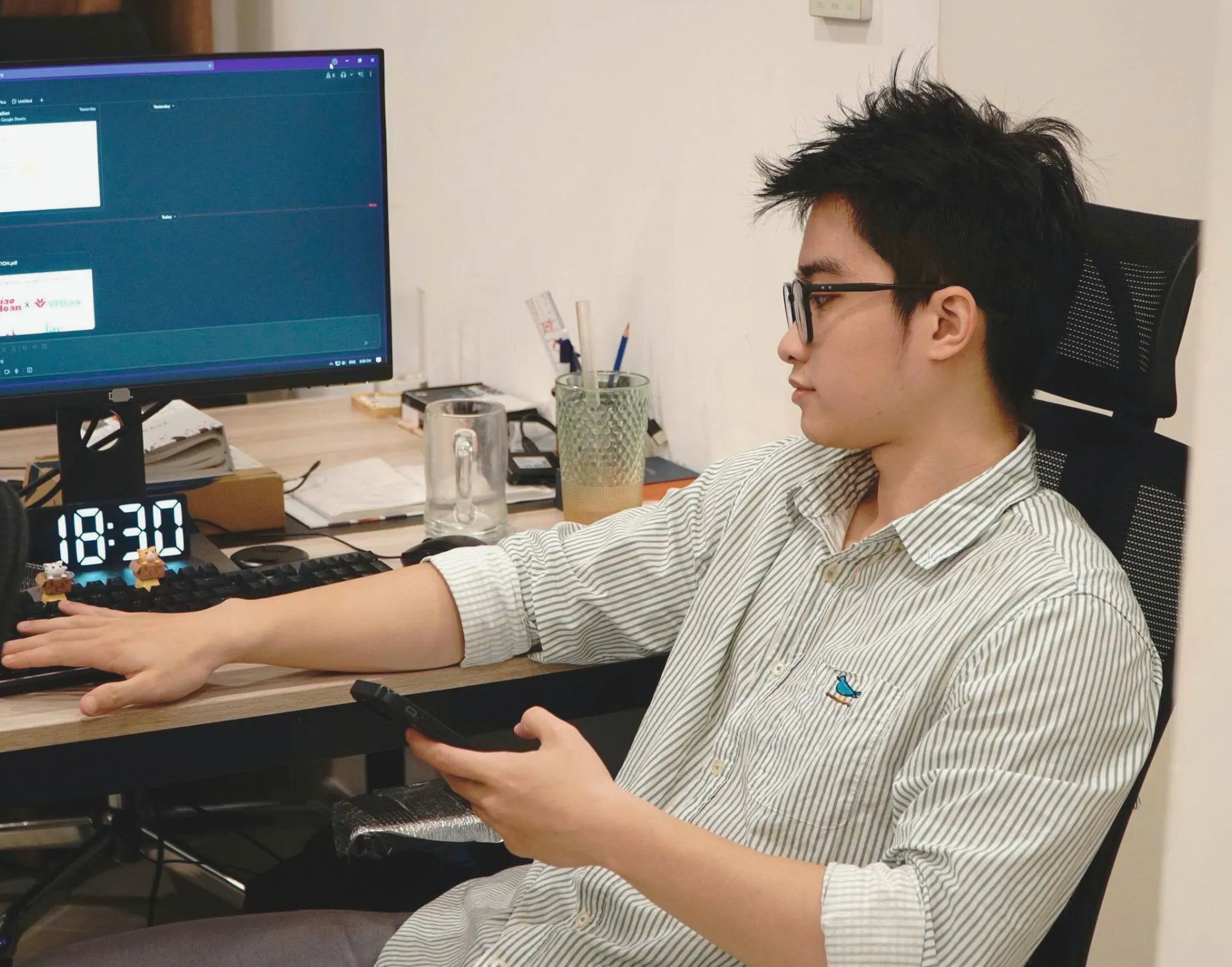 Hoàng Huy Đức at his desk, working at a monitor with a phone in his hand.