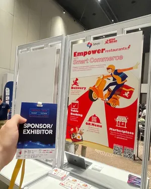 A hand holding a French Tech Summit Vietnam sponsor and exhibitor badge in front of the Savyu roll-up banner.