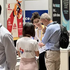 At the Savyu booth, Đức listens to a visitor with a backpack while a colleague in a Savyu T-shirt stands in front.