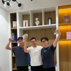 Three people celebrating at Savyu's hackathon, holding up glass trophies and prize money.