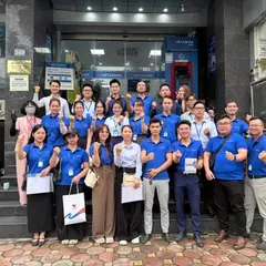 About twenty-five people, most in blue VietABank polo shirts, raising their fists on the steps outside a VietABank branch.